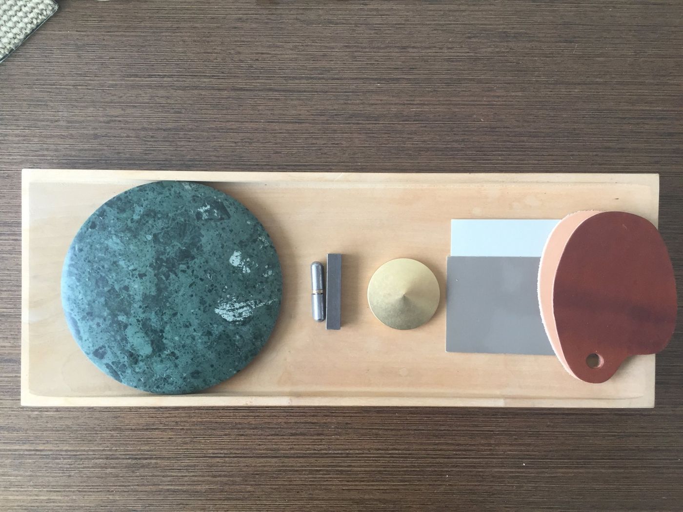 Samples on a timber board: green stone, brass, steel, grey panel and leather.