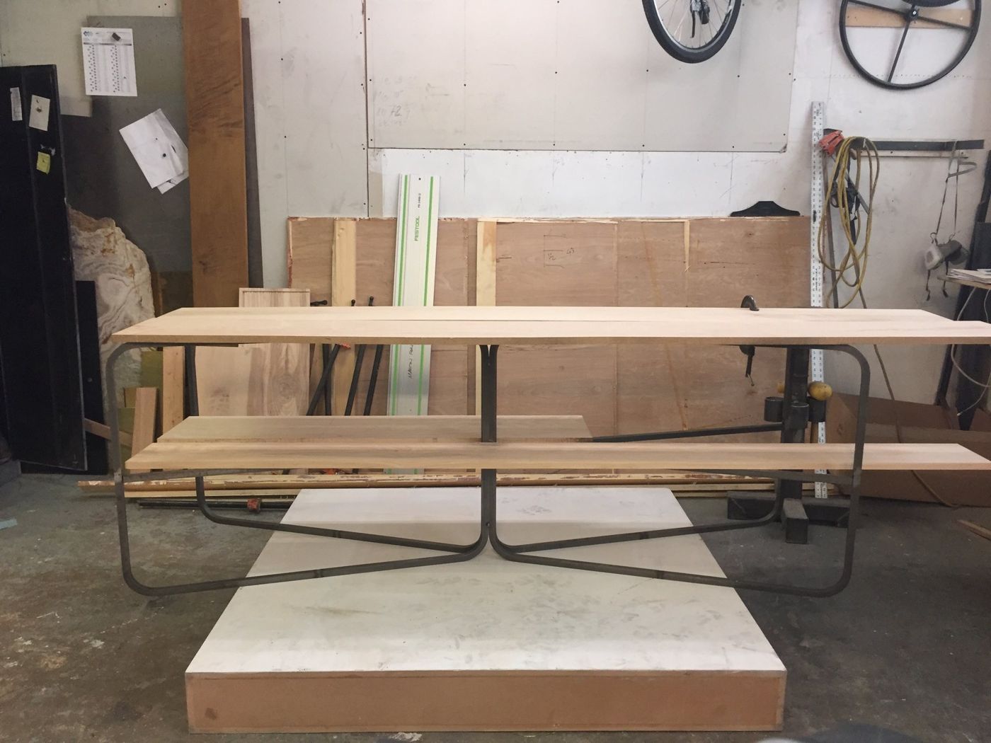 A table of ash planks on a bent steel frame, on a stand in a workshop.