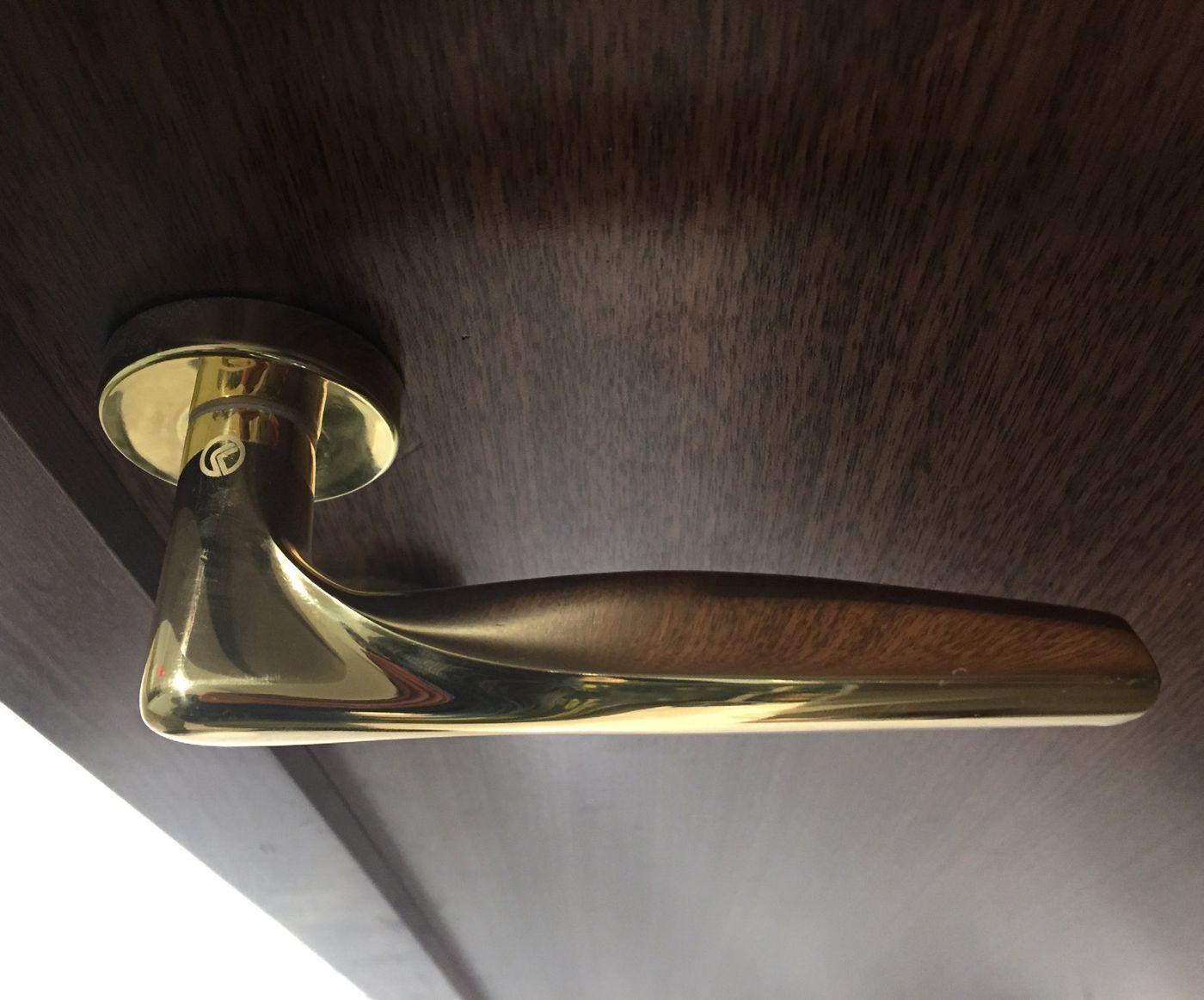 A brass-coloured lever mounted on a dark timber door, seen from above.