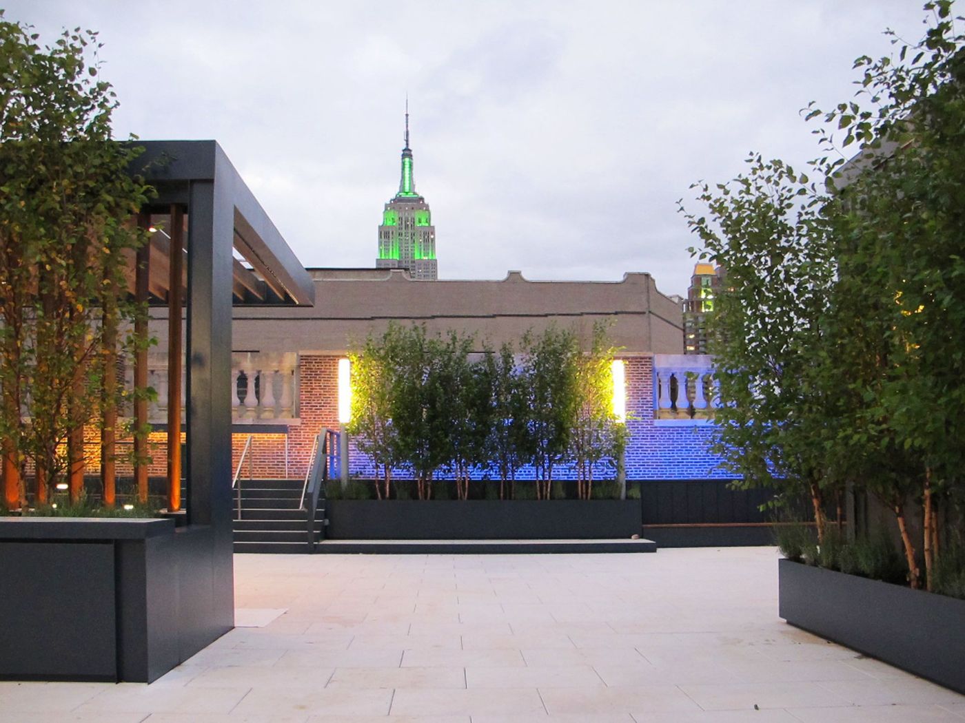 Planters and a lit parapet at dusk, the Empire State Building in green light behind.