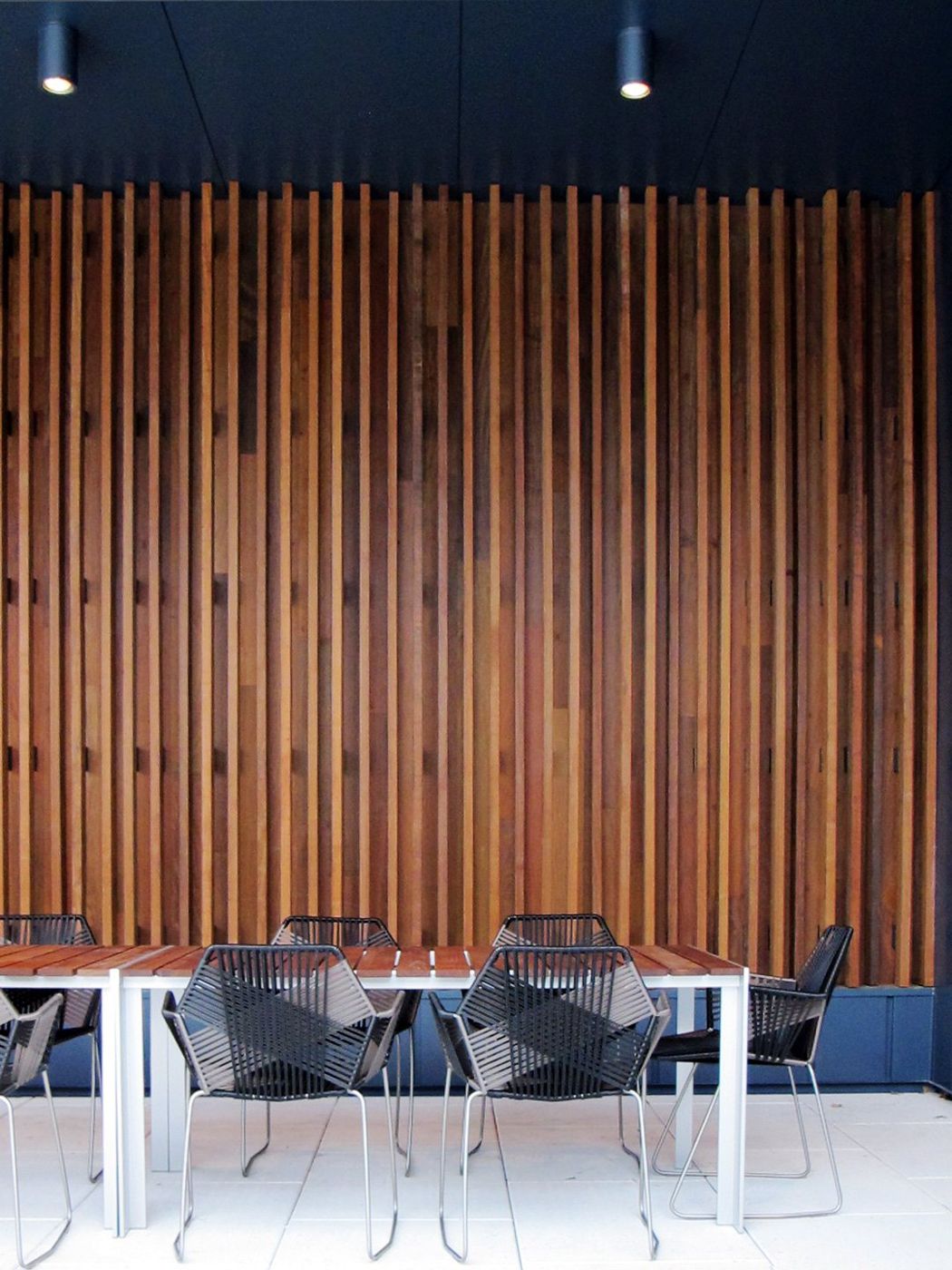 A wall of vertical timber slats behind a table with black wire chairs.