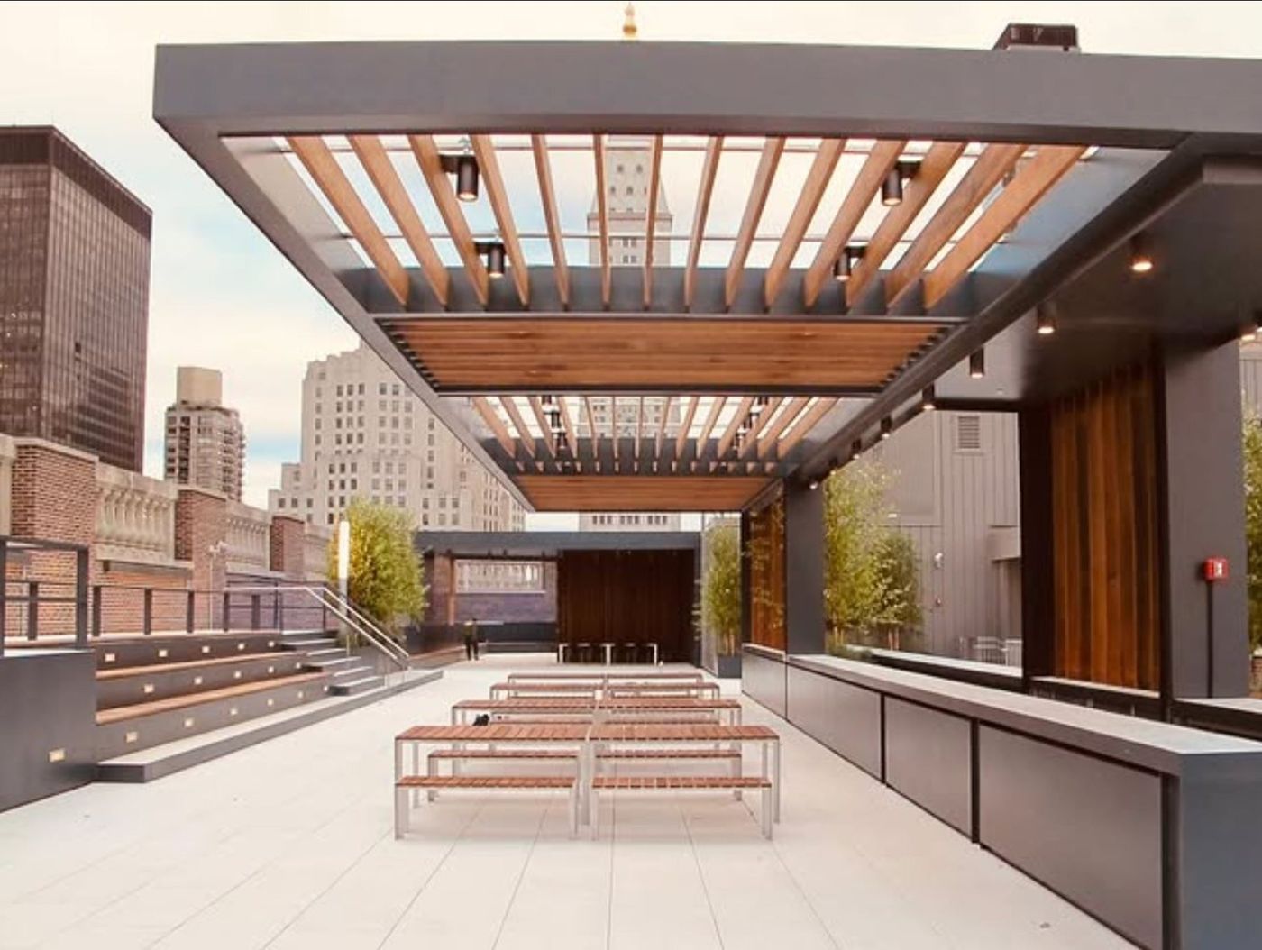 Long timber tables under the pergola's louvres, benches along the side.