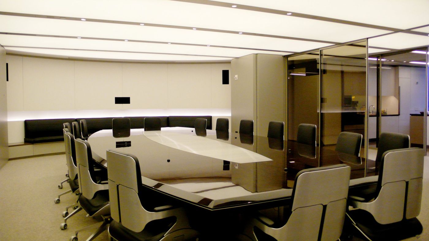 A pale oval table with high-backed chairs in a curved room lined with a dark banquette.