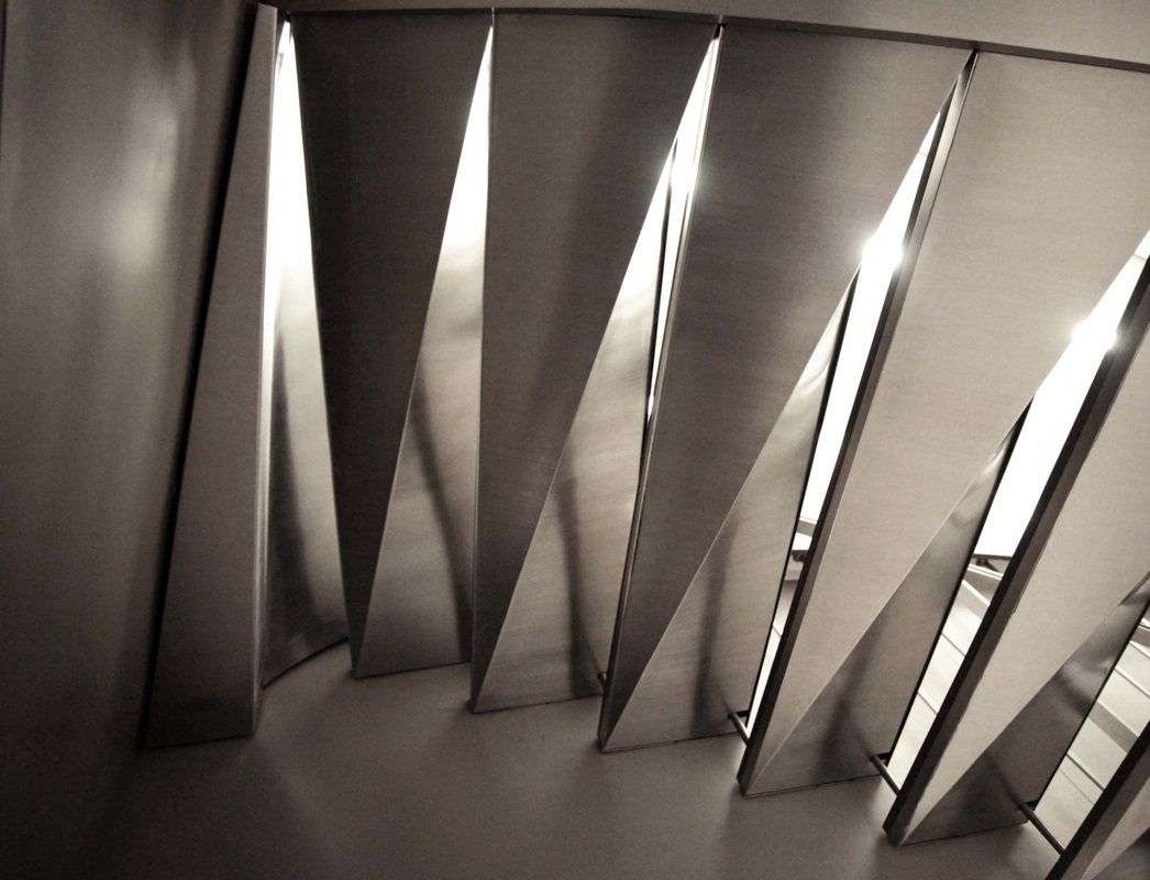 Underside of the stair: folded steel plates catch the light in a row of sharp triangles.