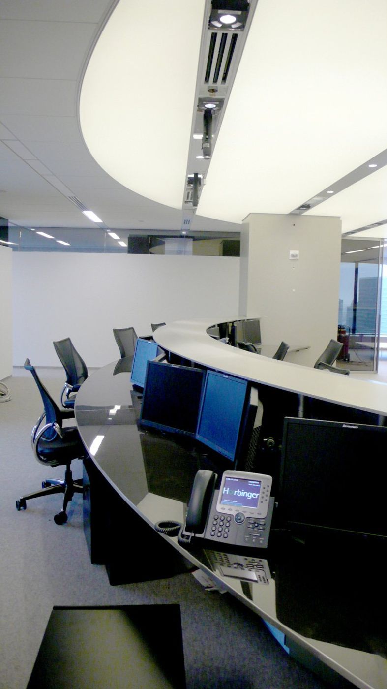 A curved run of trading desks with monitors and task chairs, seen along its length.