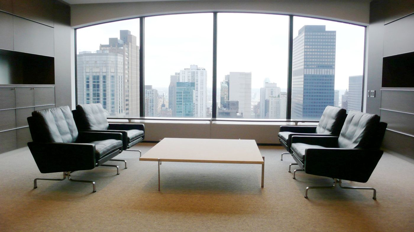 Four black leather lounge chairs and a low table before a wide window onto Midtown towers.