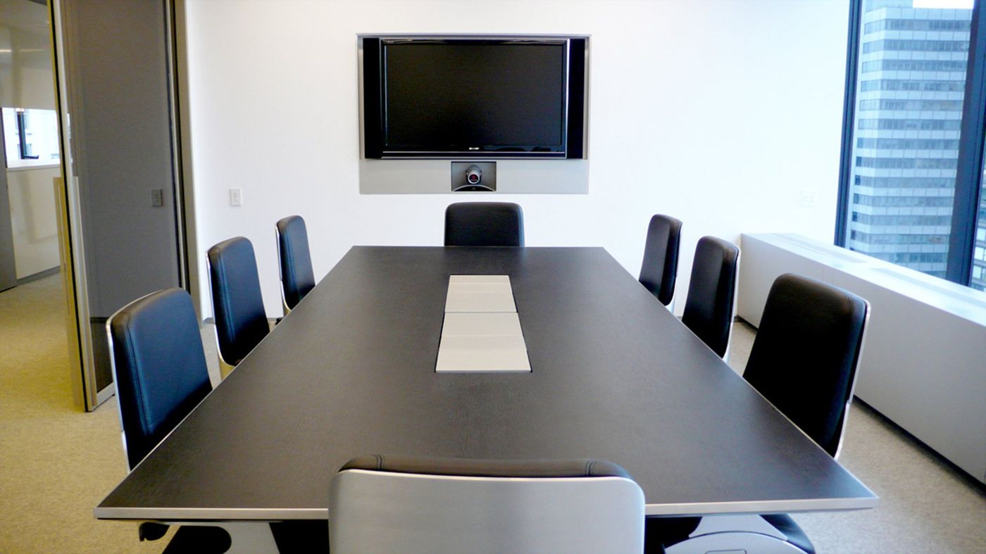 A dark rectangular table with black chairs, a screen on the end wall and a window to the right.