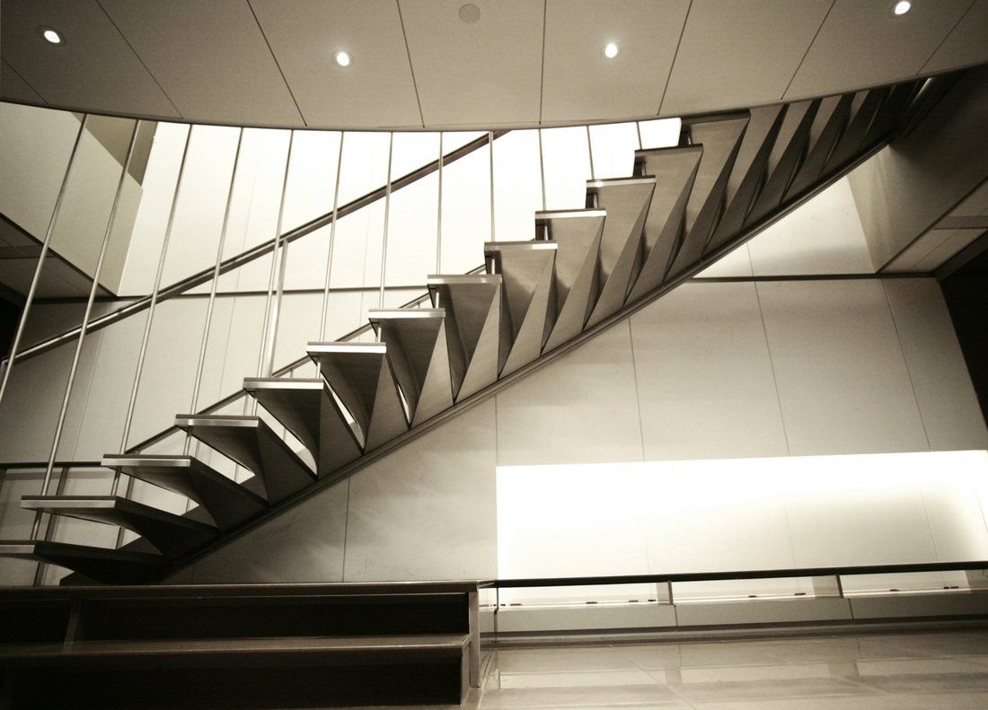 A steel stair with a folded stringer rising beneath a curved white ceiling.