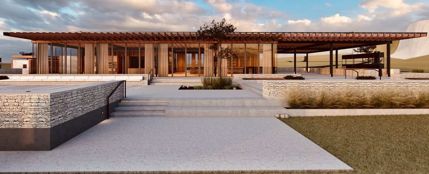 The long timber building on a stone terrace with steps and grasses in front.