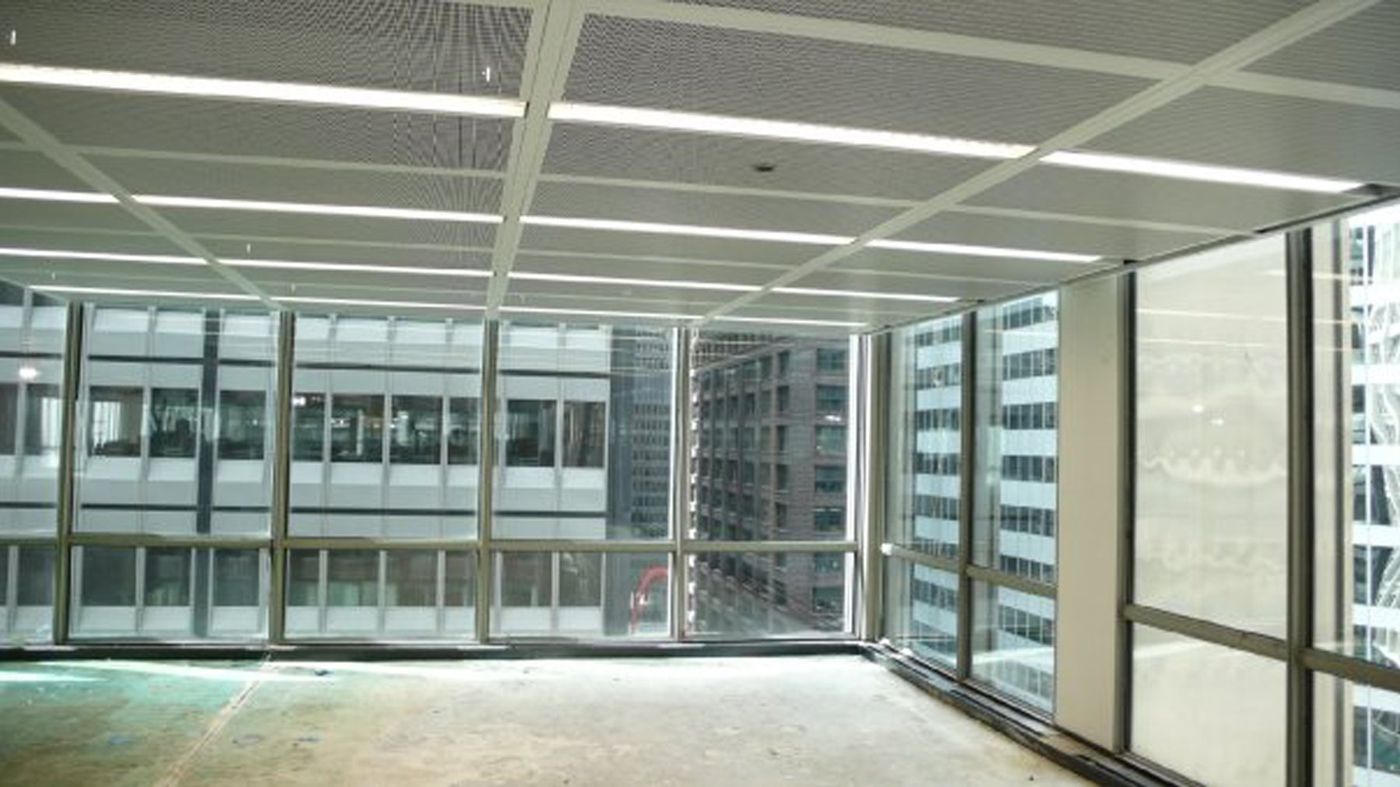 An empty office floor with a trial ceiling of perforated panels and linear lights.