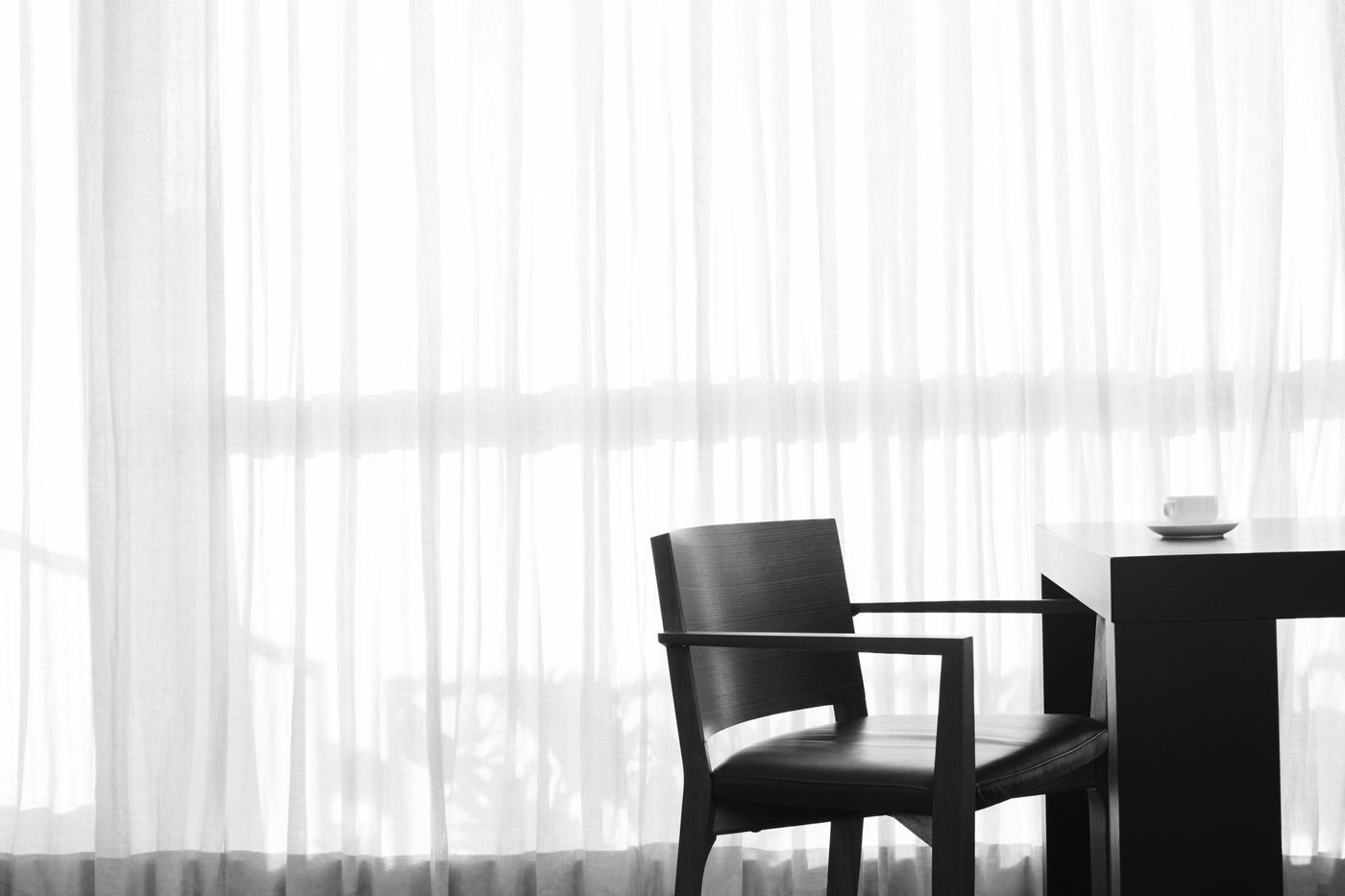 A dark timber chair and table silhouetted against white sheer curtains.