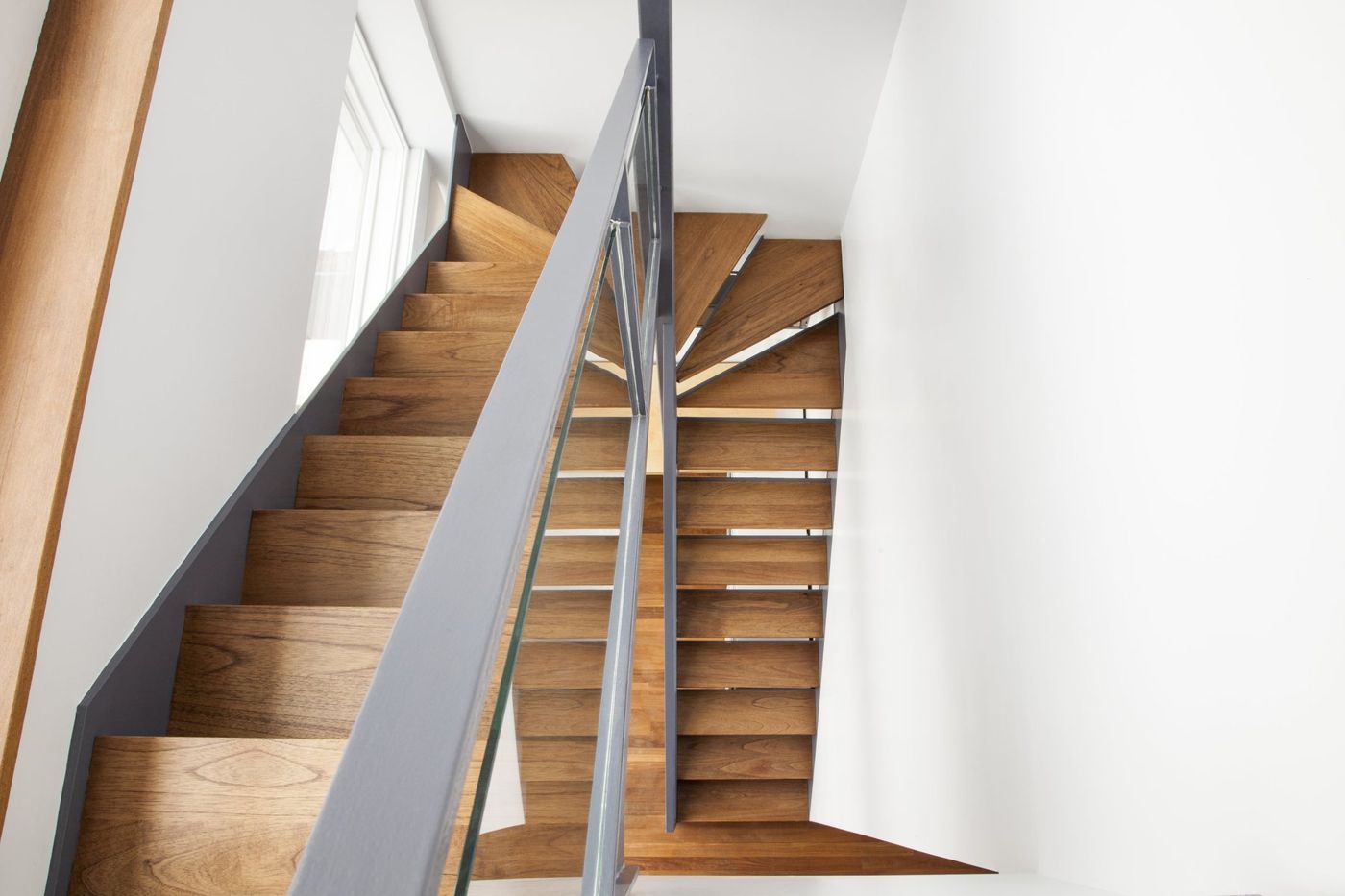 A timber stair with a steel rail turning up between white walls.