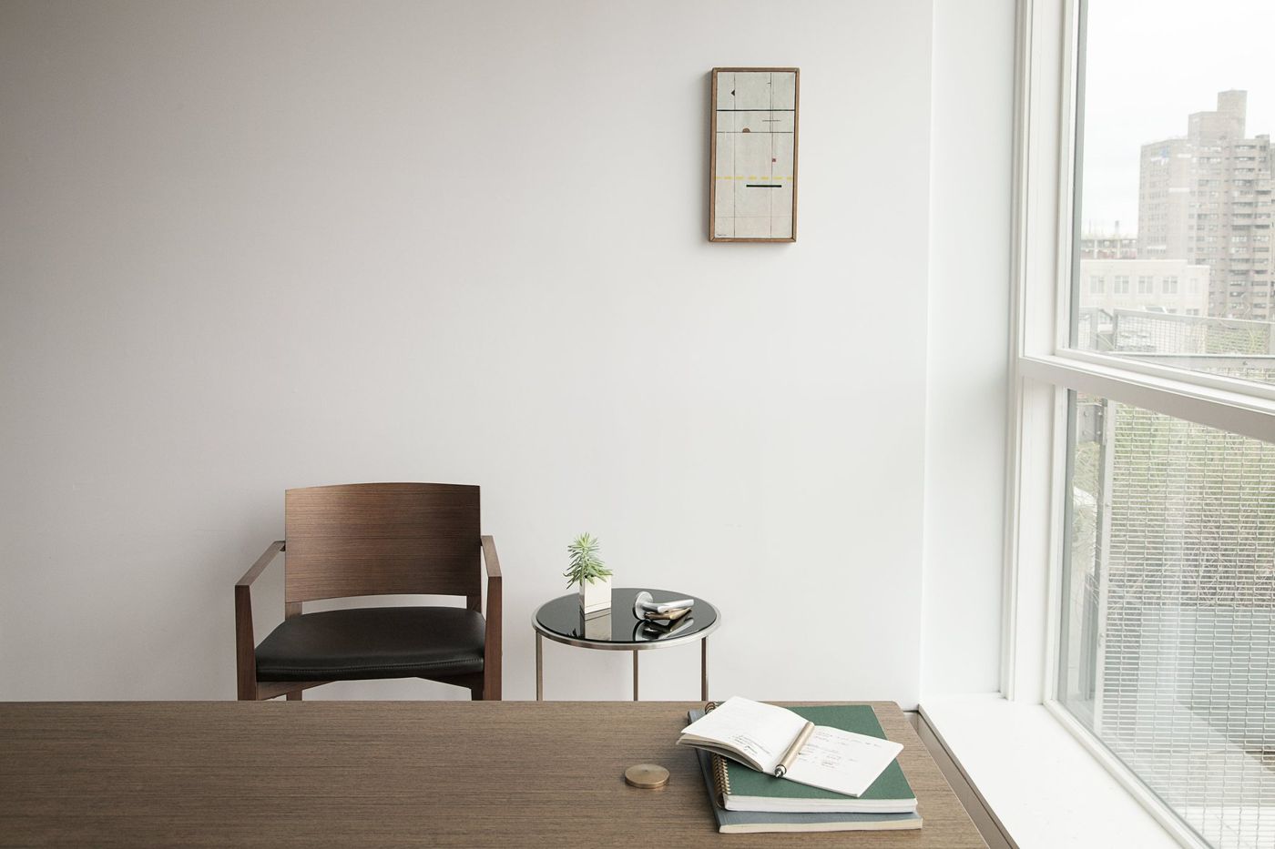 A timber chair and small side table at a desk beside a tall window.