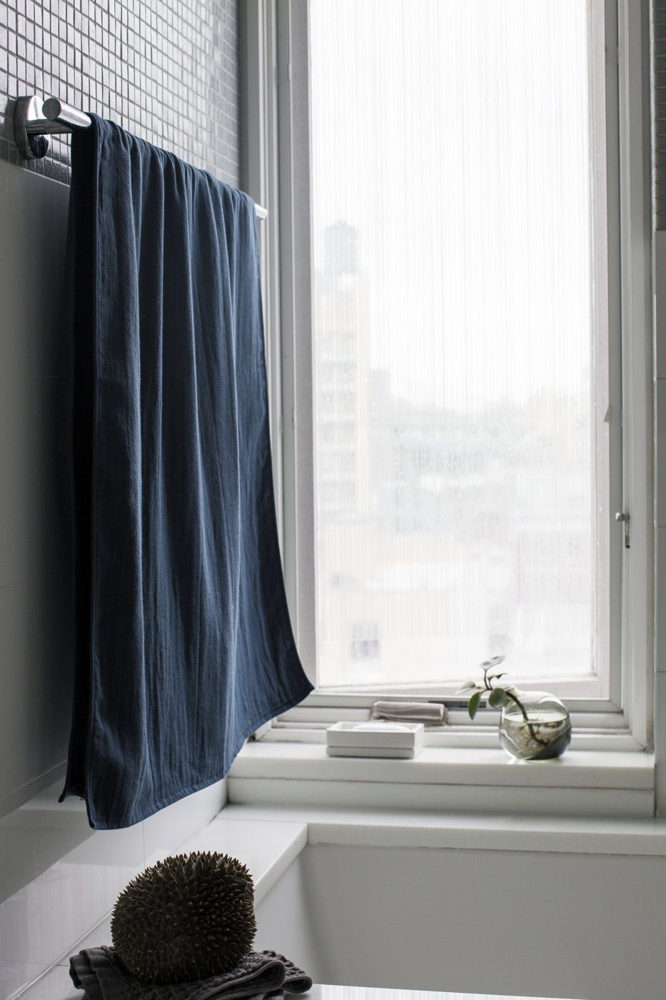 A blue towel on a rail beside a white bath and a tall window.