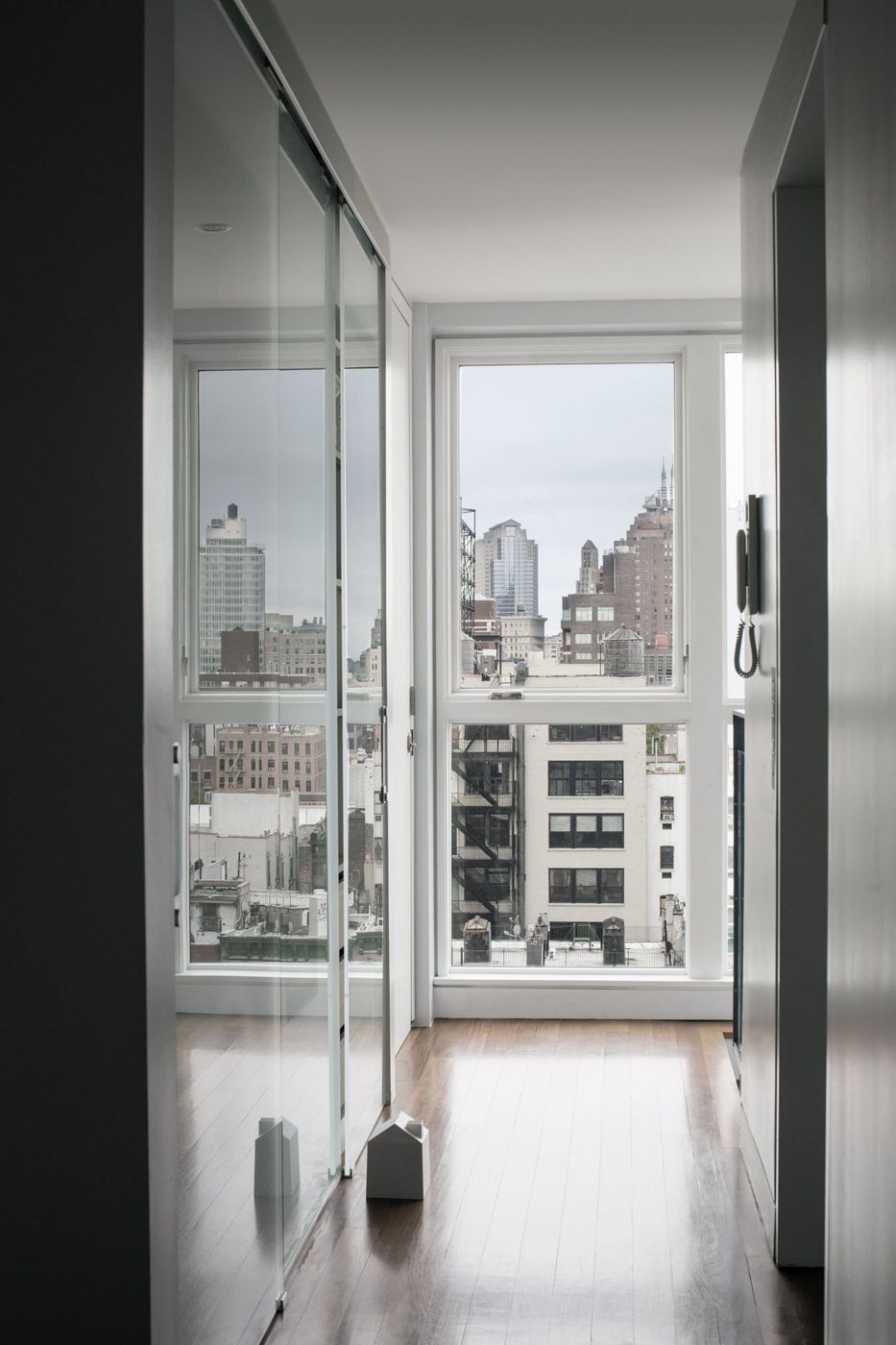 A narrow hall with glass sliding doors leading to a window onto the city.
