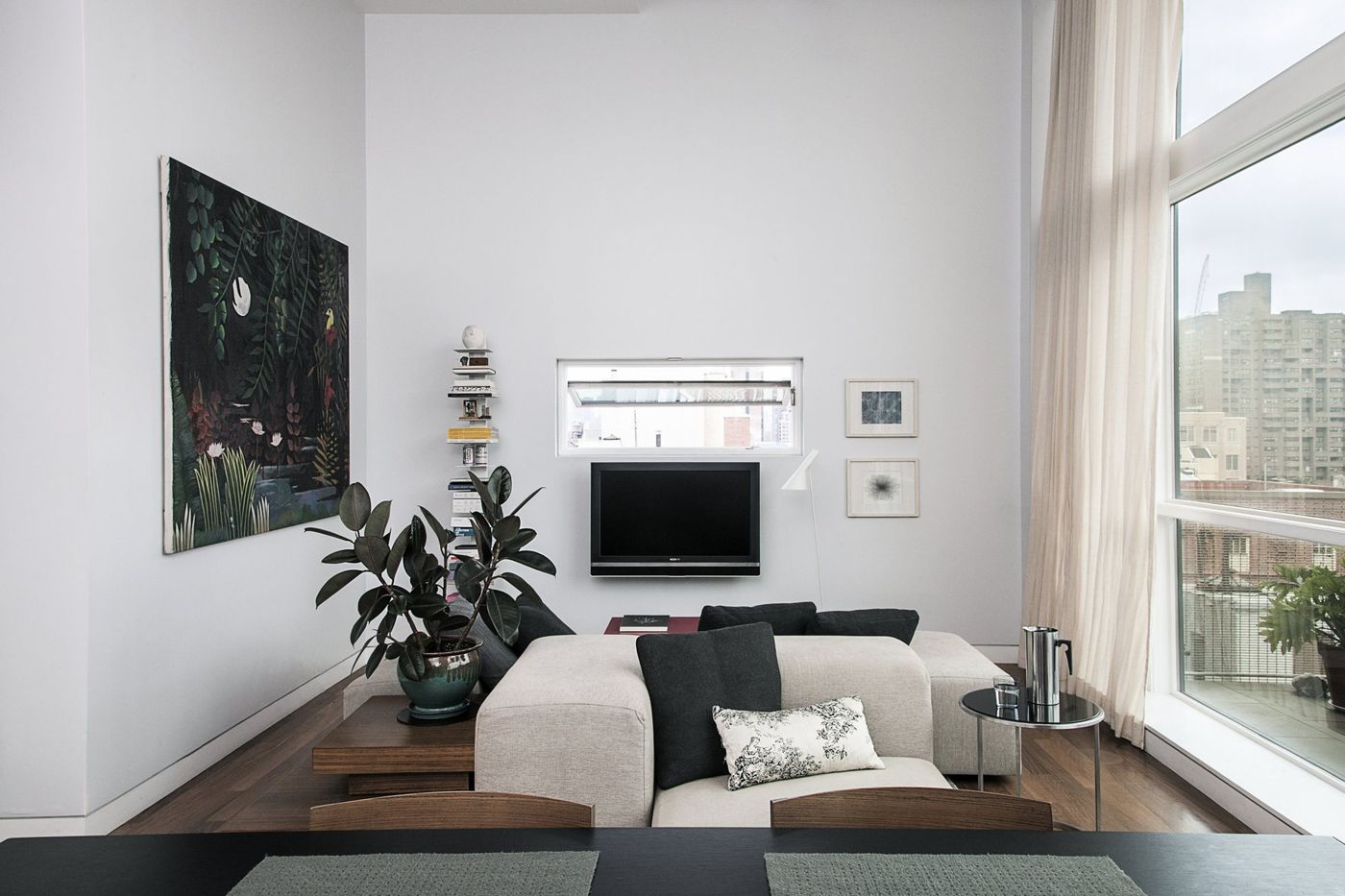A pale sofa, plants and a painting in a white living room with a full-height window.