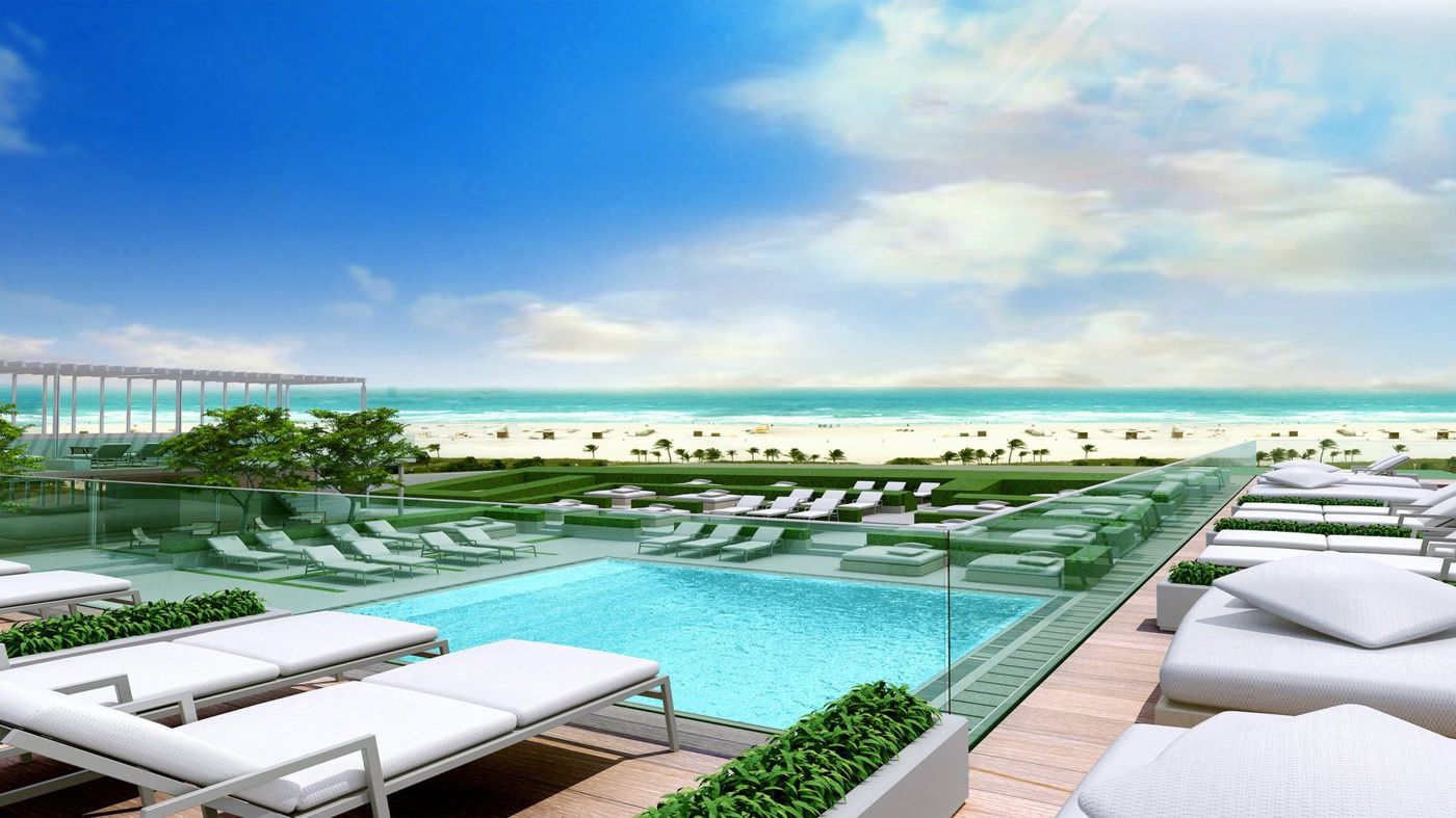 A pool deck with white loungers and a glass balustrade looking over the beach to the sea.