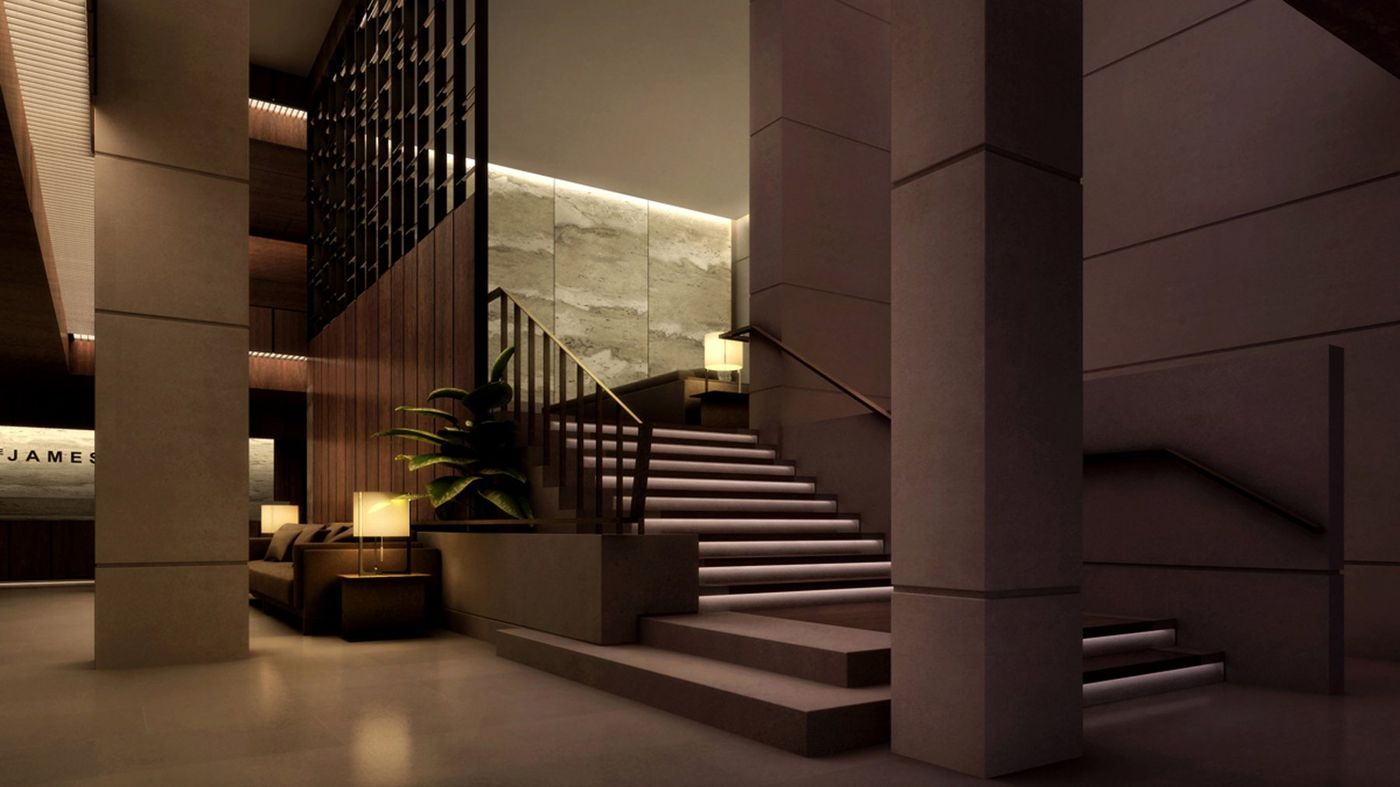 A dark reception hall with stone columns and a stair rising beside a lit stone wall.