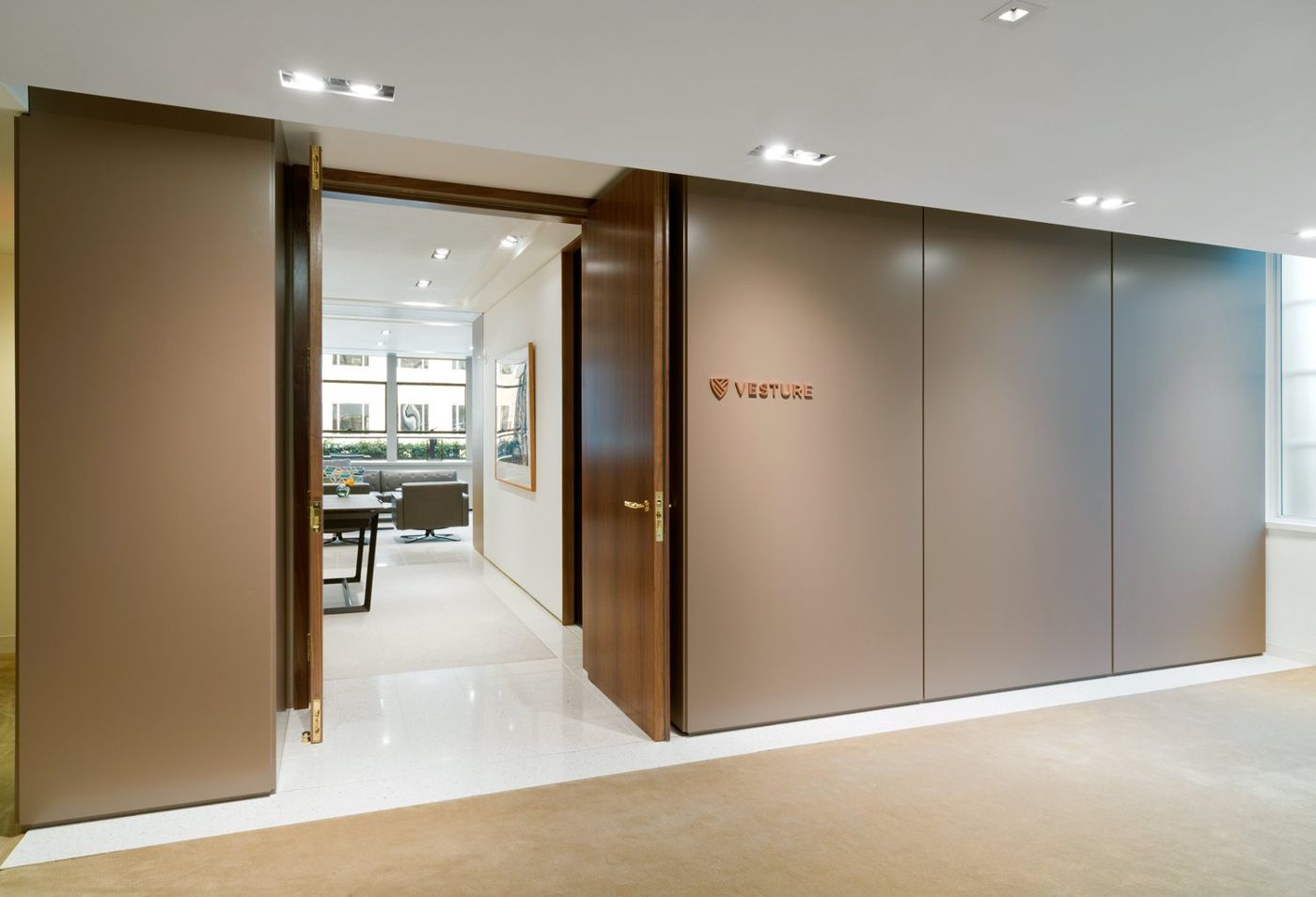 Tall timber doors stand open in a wall of taupe panels, the studio visible beyond.