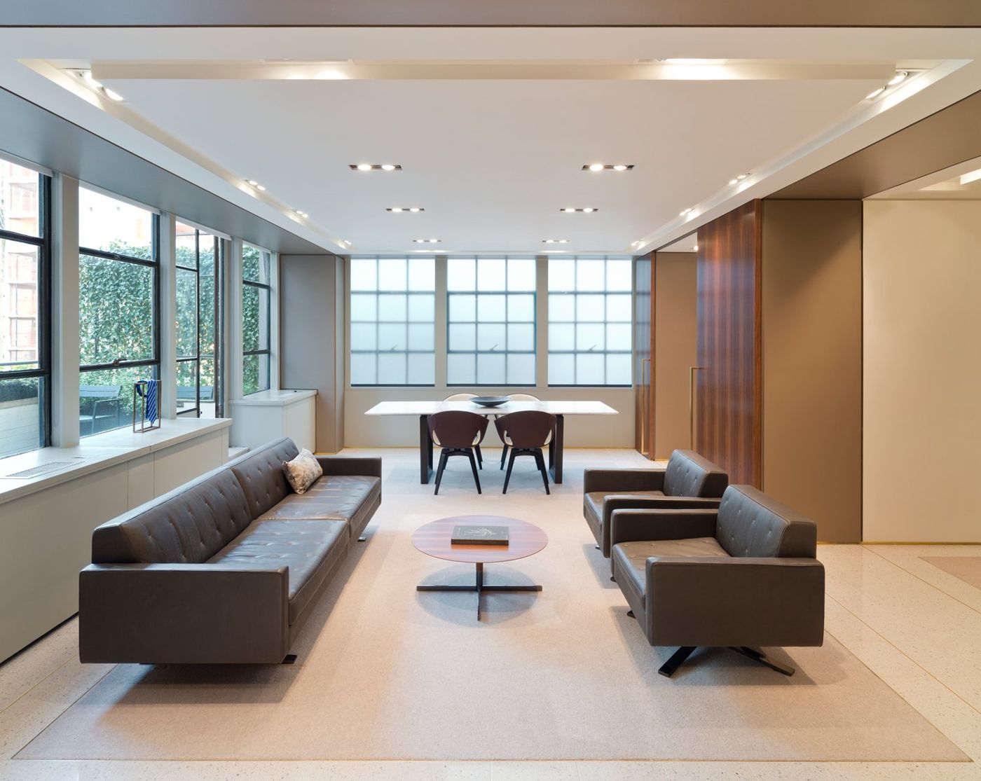 Grey leather sofas and chairs around a round timber table, a dining table by the windows.