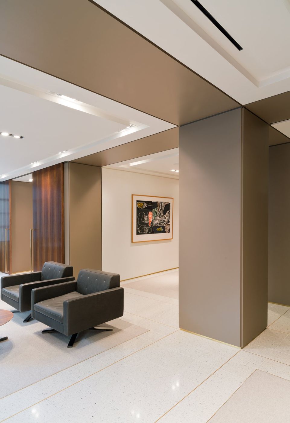 A taupe column casing meets a stepped ceiling above and a terrazzo floor with brass inlay.