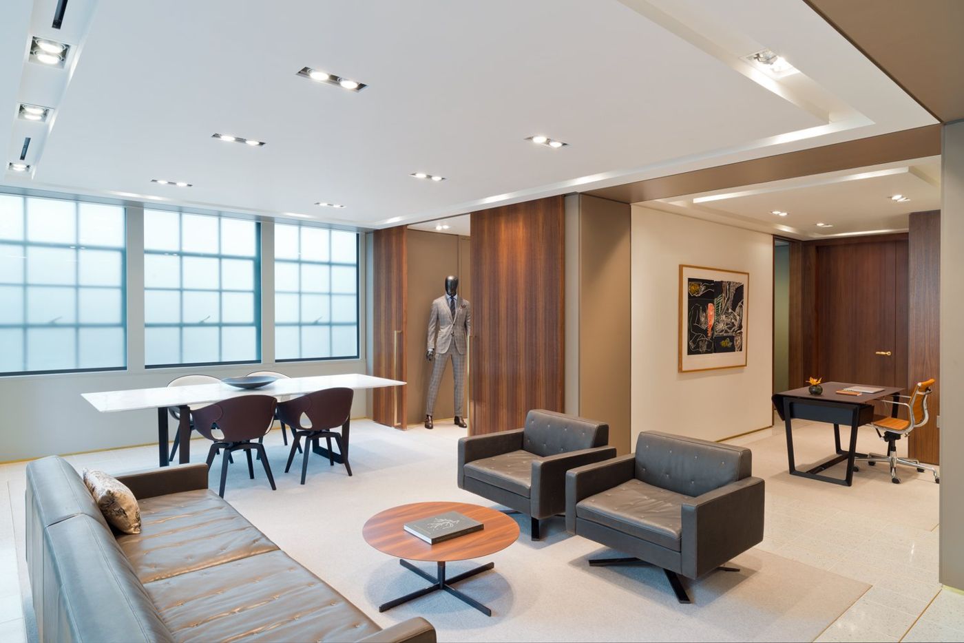 Lounge chairs and a dining table in front of walnut panels, a tailor's dummy by the window.