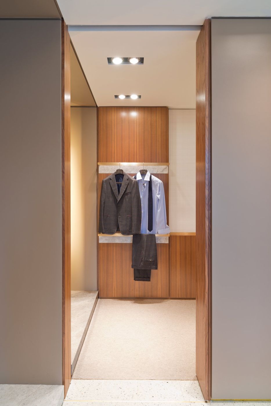 A narrow dressing room lined in walnut, a jacket and shirt hung on the back wall.