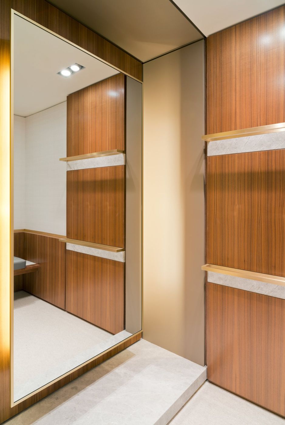 A full-height mirror reflecting walnut panels with brass and stone rails.